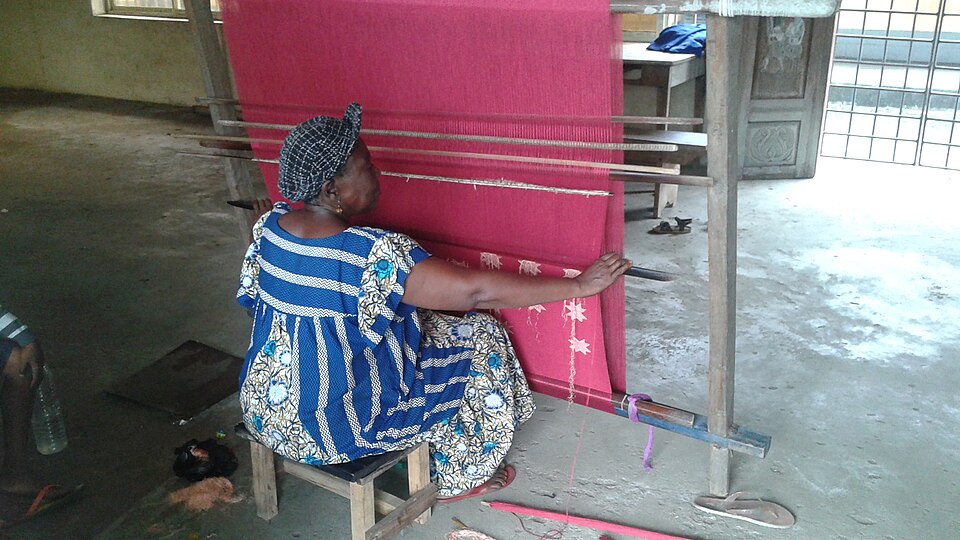 Akwete — Akwete weaving on a vertical loom, Nigeria, 2017 — photo: OBankz (Ekekeh Ubadire Obioma) — Wikimedia Commons / CC BY-SA 4.0